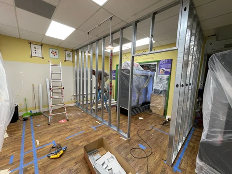 Perfilería metálica de una división interior junto a las marcas de cinta azul y materiales de trabajo.