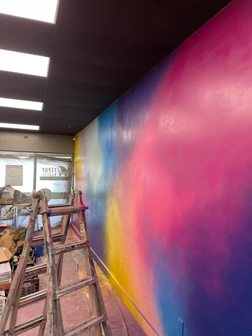 Pared interior con zonas de color azul, rosa y amarillo durante el trabajo, junto a una escalera y bajo el techo negro.