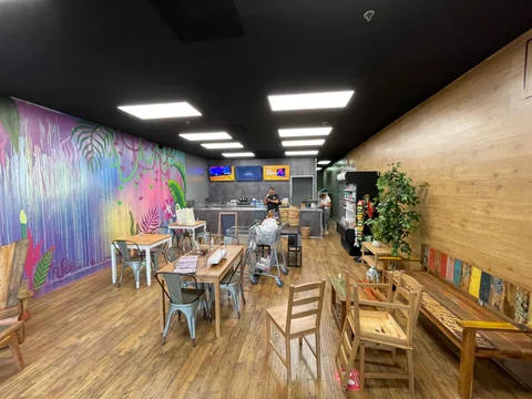 Vista amplia del local de açaí bowls con mural colorido, mesas y sillas, pared de madera y mostrador al fondo durante la puesta a punto.