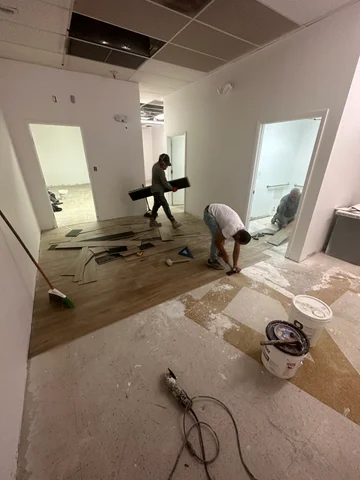 Workers installing flooring in the rear area of the space, with tools and materials around them.