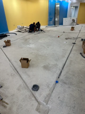 Channels and installed components in the main room floor during construction, with workers in the background.