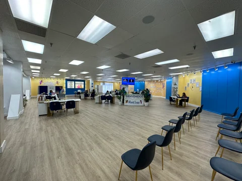 The main room in use, with wood-look flooring, blue chairs, service desks and reception at the far end.