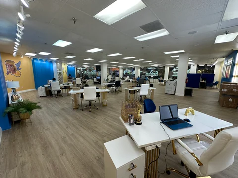 Reverse view of the main room with service desks, white furniture, blue panels and glazing in the background.