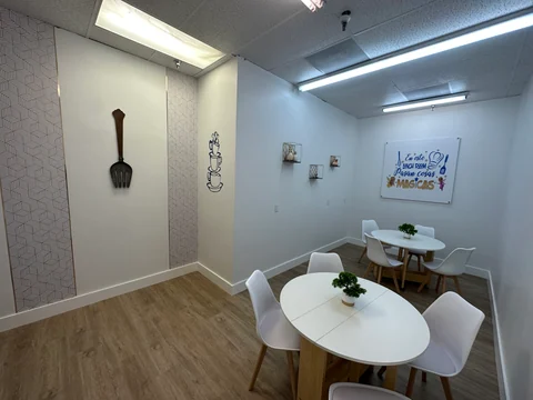 Break room with white tables, light chairs, wood-look flooring and wall decorations.