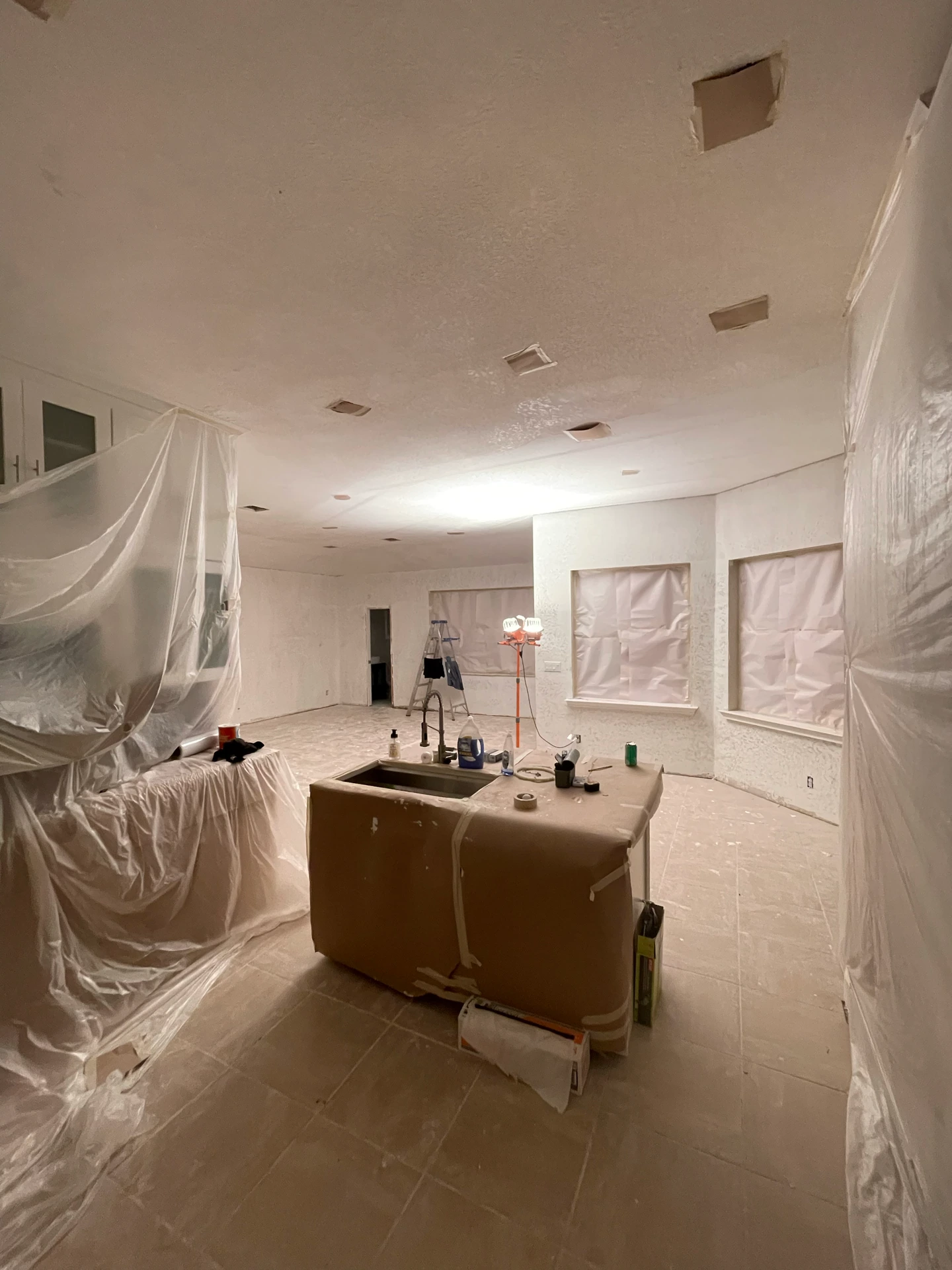 Kitchen in the Boca Ratón home with cabinets and windows protected, a work light and surfaces being prepared.