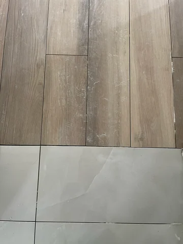Detail of the transition between wood-look floor tiles and larger light-colored tiles.