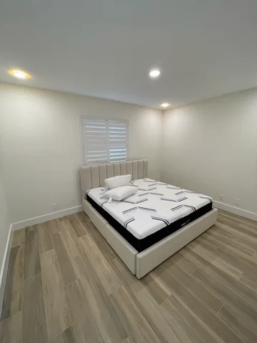 Bedroom with wood-look flooring, light-colored walls, a bed and a shuttered window.