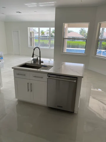 Kitchen island with a sink, faucet and dishwasher, facing windows overlooking the garden.
