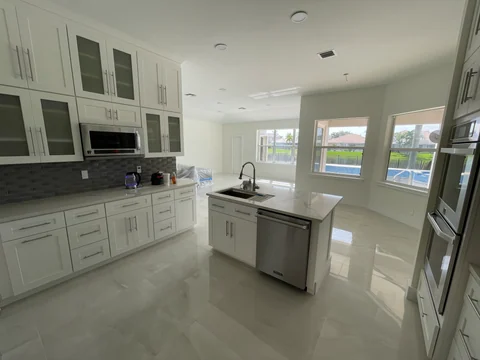 Wide view of the kitchen with white cabinets, an island and light flooring, connected to the living space.