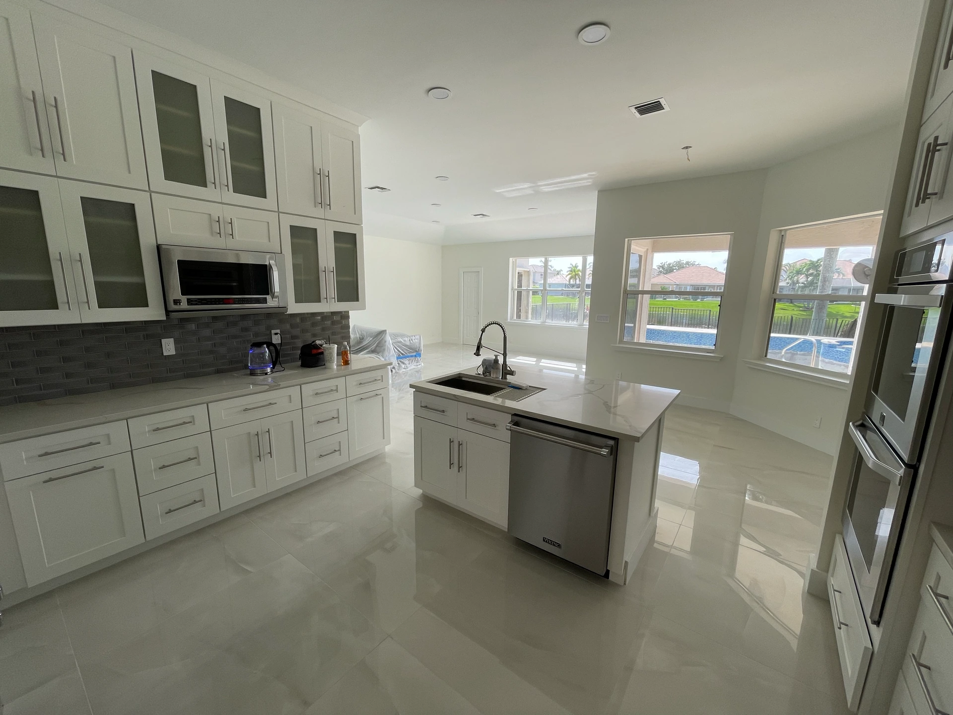 Wide view of the kitchen with white cabinets, an island and light flooring, connected to the living space.