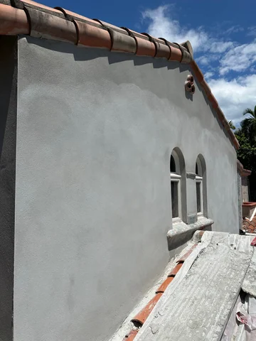 An exterior wall with gray coating, small arched windows and a tiled roof above.