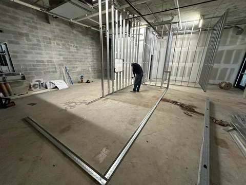 A worker beside the metal partition framing, with materials and tools on the construction floor.