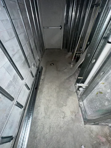 Interior passage during construction, with metal partition framing, visible connections and an unfinished floor.