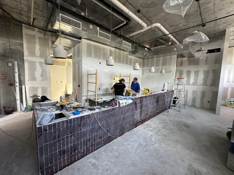 Bar during finishing work, with reddish ceramic facing, workers and materials on the surface.