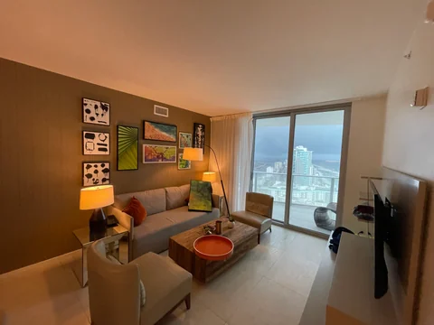 Living room before the flooring change, with a sofa, coffee table, wall art and glazing toward the balcony.