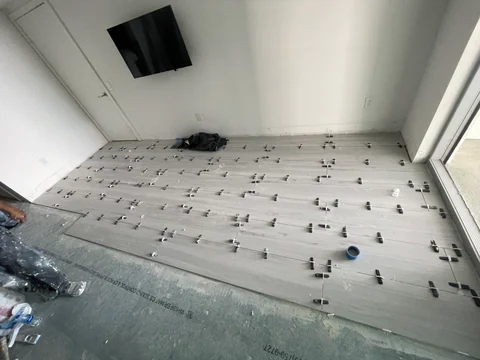 Light-colored flooring during installation, with leveling clips and a section of the base still exposed.