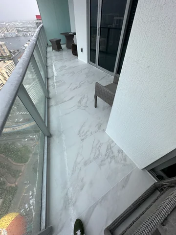 Light, gray-veined flooring installed on the balcony beside the glass railing and sliding doors.