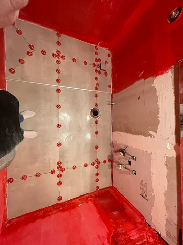 Shower during tilework, with red waterproofing, installed tiles and leveling clips.