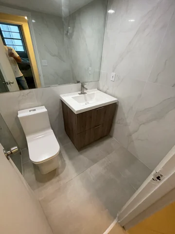 Bathroom with light, gray-veined walls, a floating wood vanity, white basin, mirror and toilet.