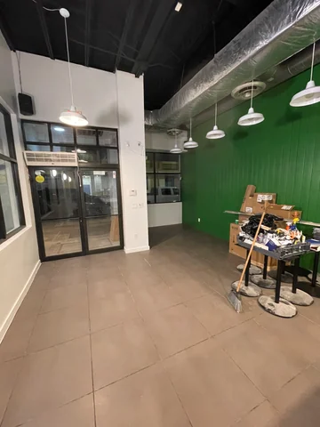 Acceso acristalado de Smile Empanadas junto a la pared verde, luminarias colgantes y materiales de trabajo.