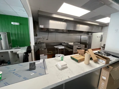 Cocina de Smile Empanadas vista desde el mostrador, con campana, equipamiento y superficies aún con protecciones y cajas.
