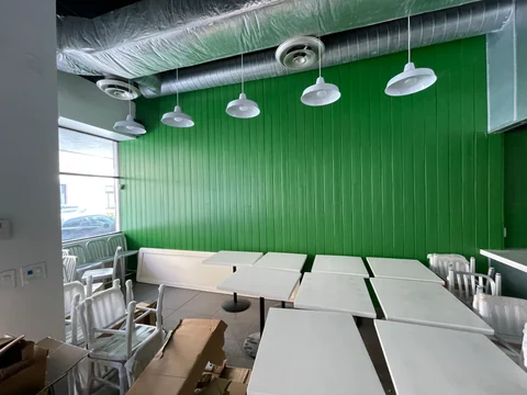 Mesas, banco y sillas junto a la pared verde de Smile Empanadas, con lámparas colgantes y embalajes visibles.