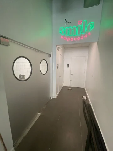 Cartel luminoso de Smile Empanadas sobre el pasillo interior, junto a dos ventanas circulares y puertas blancas.