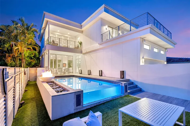 Washington exterior at dusk, with a white facade, terraces, large windows and an illuminated pool.