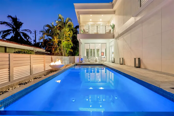Night view along Washington’s blue-lit pool, with the home’s large windows in the background.