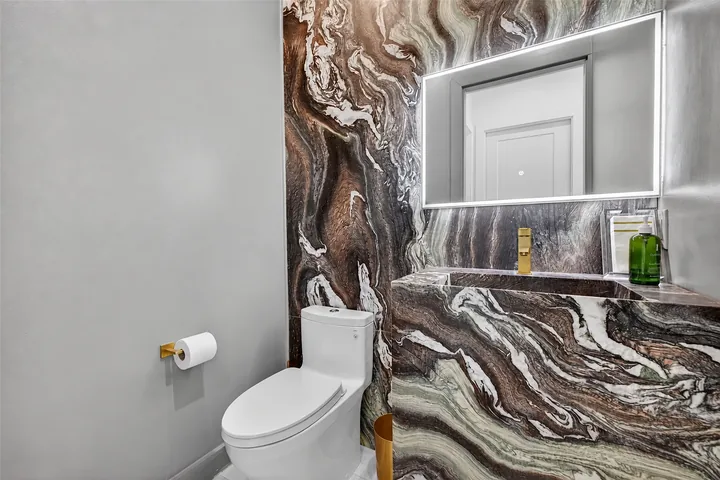 Washington powder room with a boldly veined wall and vanity surface, an integrated basin and an illuminated mirror.