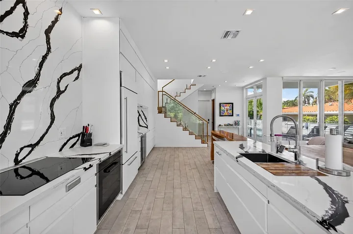 View through Washington’s kitchen between the cabinet wall and island, with white, black-veined surfaces and the staircase beyond.