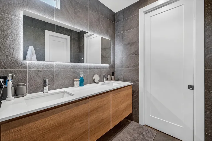 Washington bathroom with a double vanity, floating wood cabinet, wide illuminated mirror and gray walls.