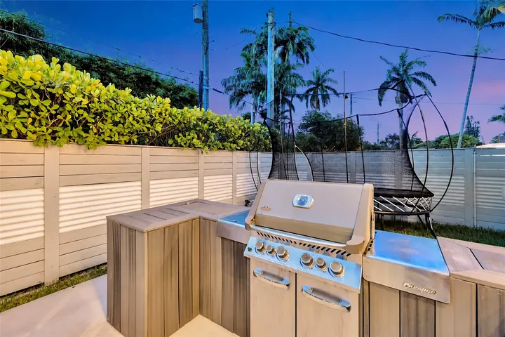 Washington outdoor area with a built-in grill between cabinets, light fencing and greenery at dusk.