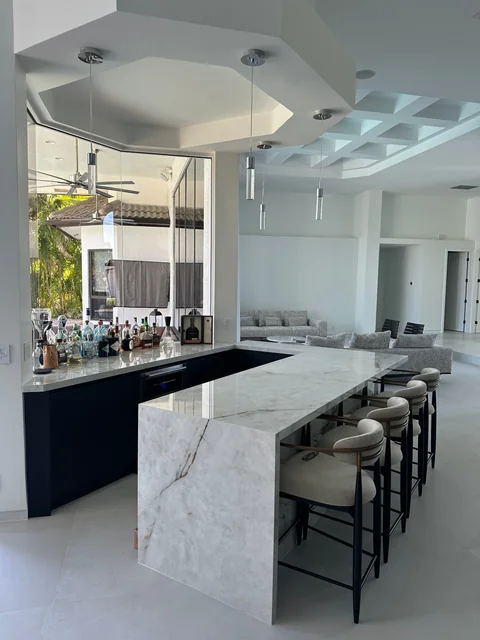 Light-surfaced bar at Weston Hills, with seating, pendant lights and an open connection to the living area.