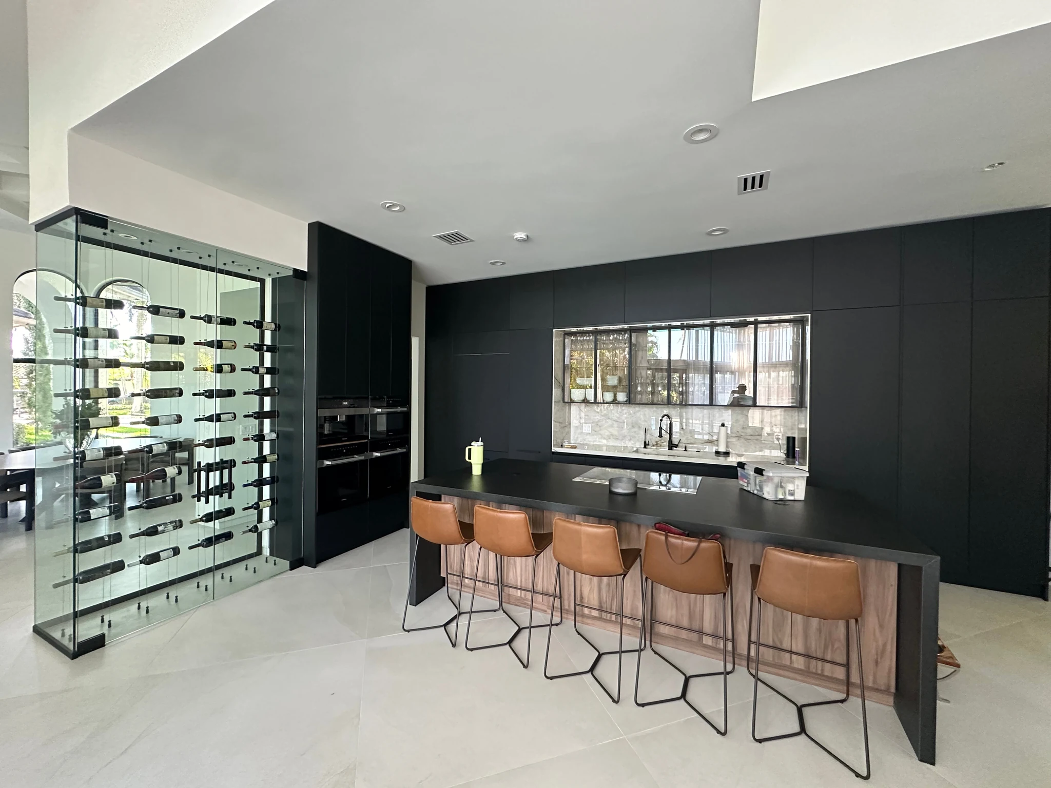 Wide view of the Weston Hills kitchen, with a dark island, brown seats, light flooring and natural light.